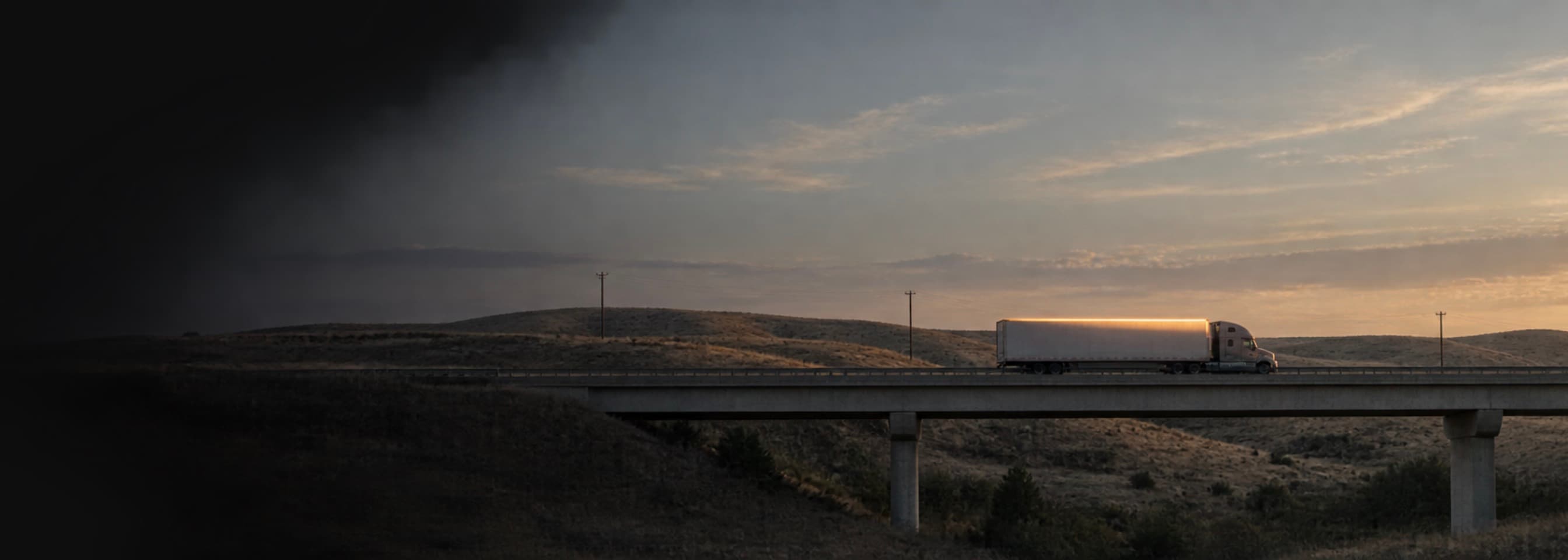 A truck crossing a highway overpass at dusk